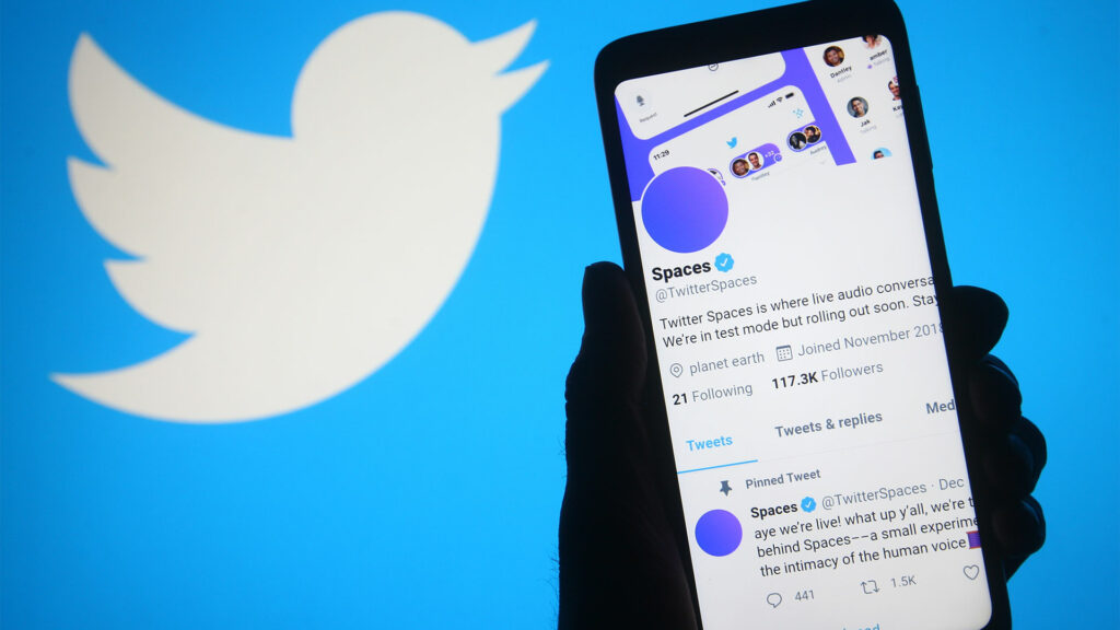 Person holding smartphone with Twitter Space on screen and large Twitter logo in background