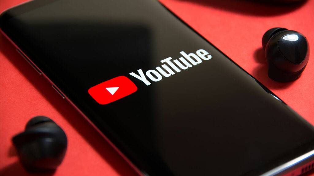 Smartphone with YouTube logo and wireless earphones next to phone